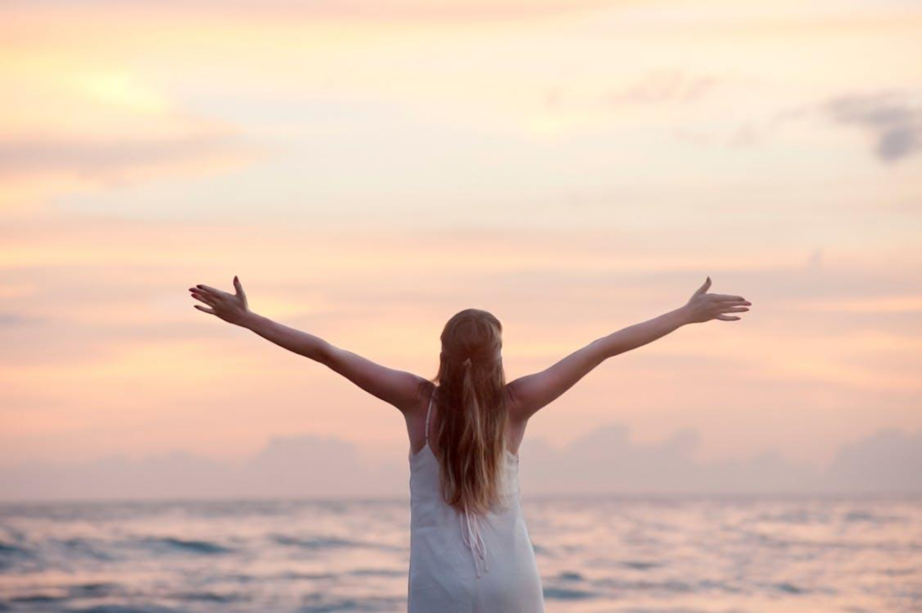 A woman spreading her arms out while looking at the sea