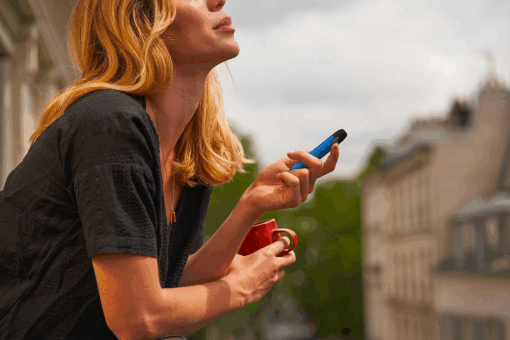 A picture of a person using a vape while holding a mug