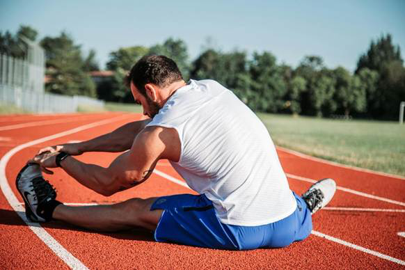 Man stretching his leg on a running track under clear skies.
