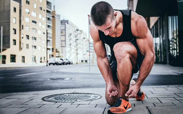 Man tying his running shoes on a city sidewalk, preparing for a workout.