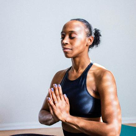 Woman meditating with eyes closed, hands together in a calm indoor setting.
