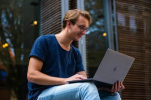Young man sitting outdoors using a laptop to explore digital art.
