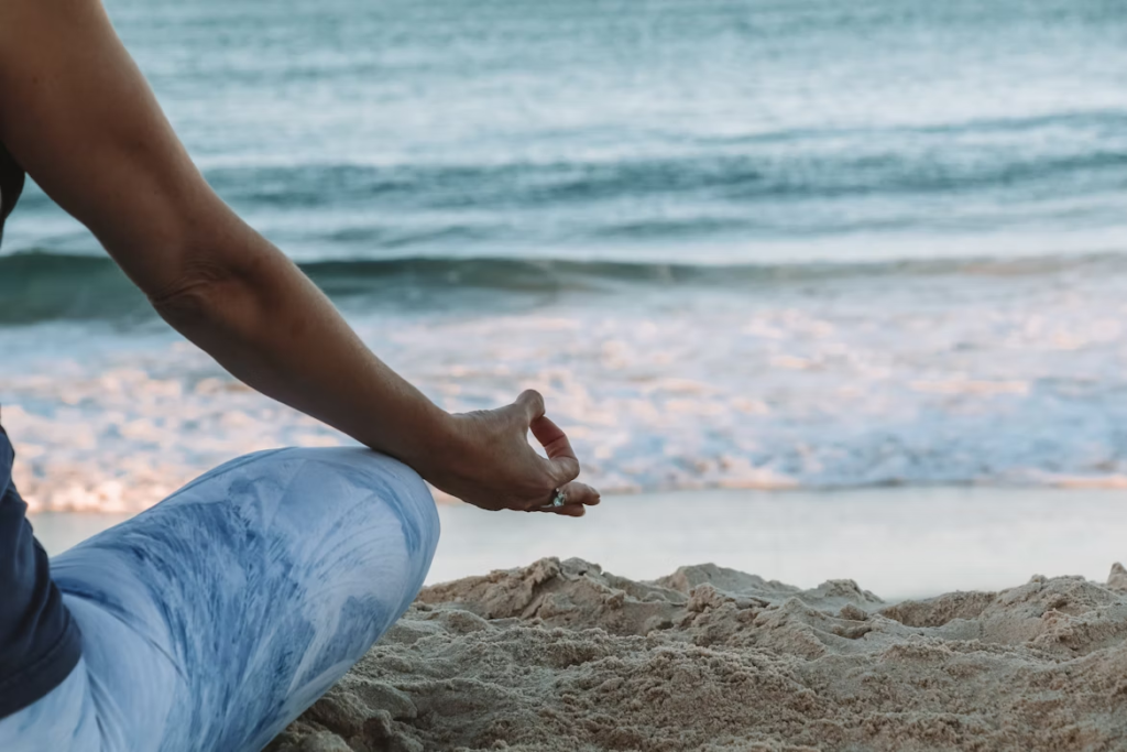 Person meditating on a peaceful beach at sunset representing mindfulness and inner calm