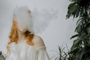 Red-haired woman behind a cloud of smoke in soft lighting