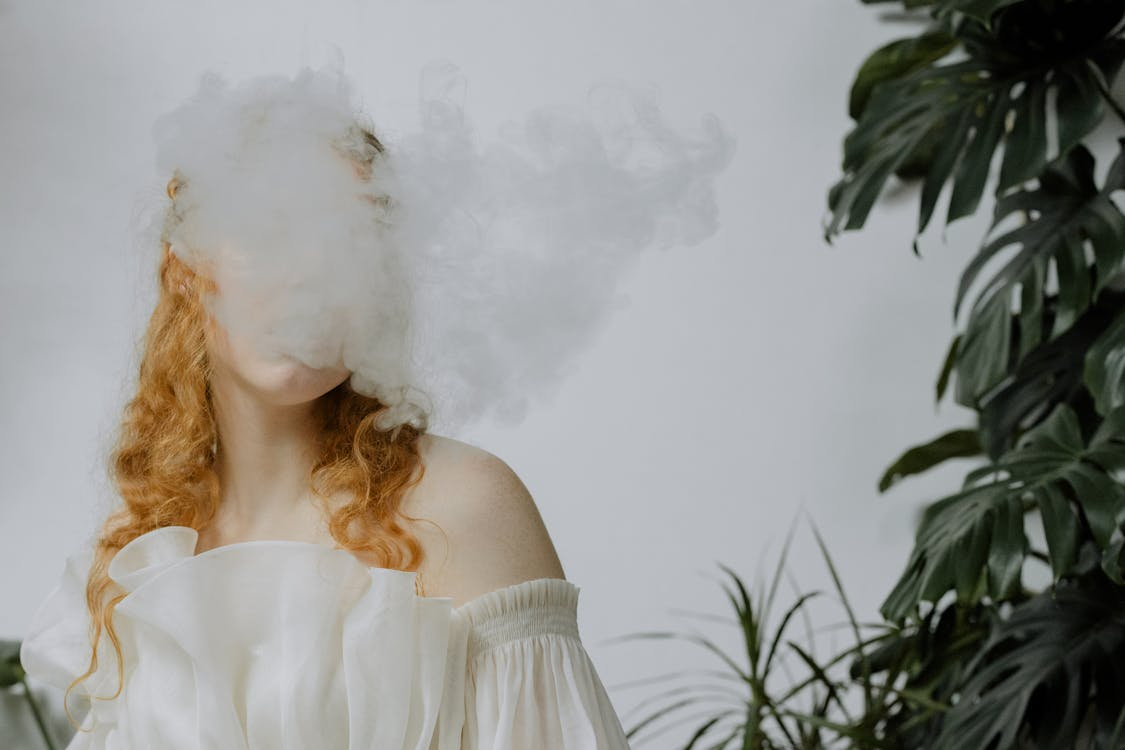Red-haired woman behind a cloud of smoke in soft lighting