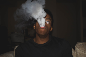 Man exhaling smoke while wearing a black crew-neck shirt
