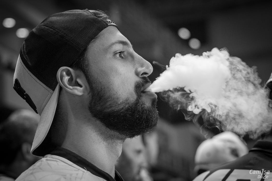 Black-and-white image of a man wearing a cap with smoke near his mouth.
