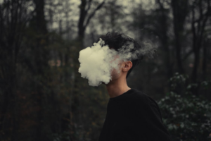 Man standing in low light with smoke around his face.