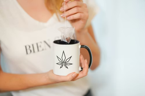 An image of a woman drinking tea in a mug with a cannabis leaf drawn on it