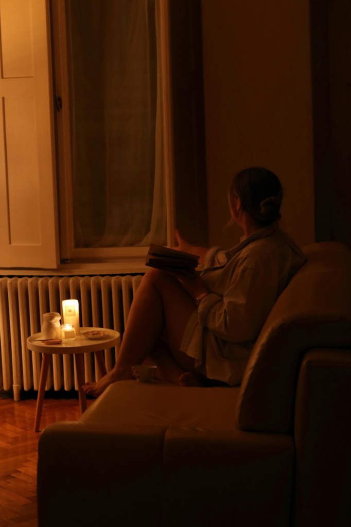 Person reading quietly beside warm candlelight in a dimly lit living room