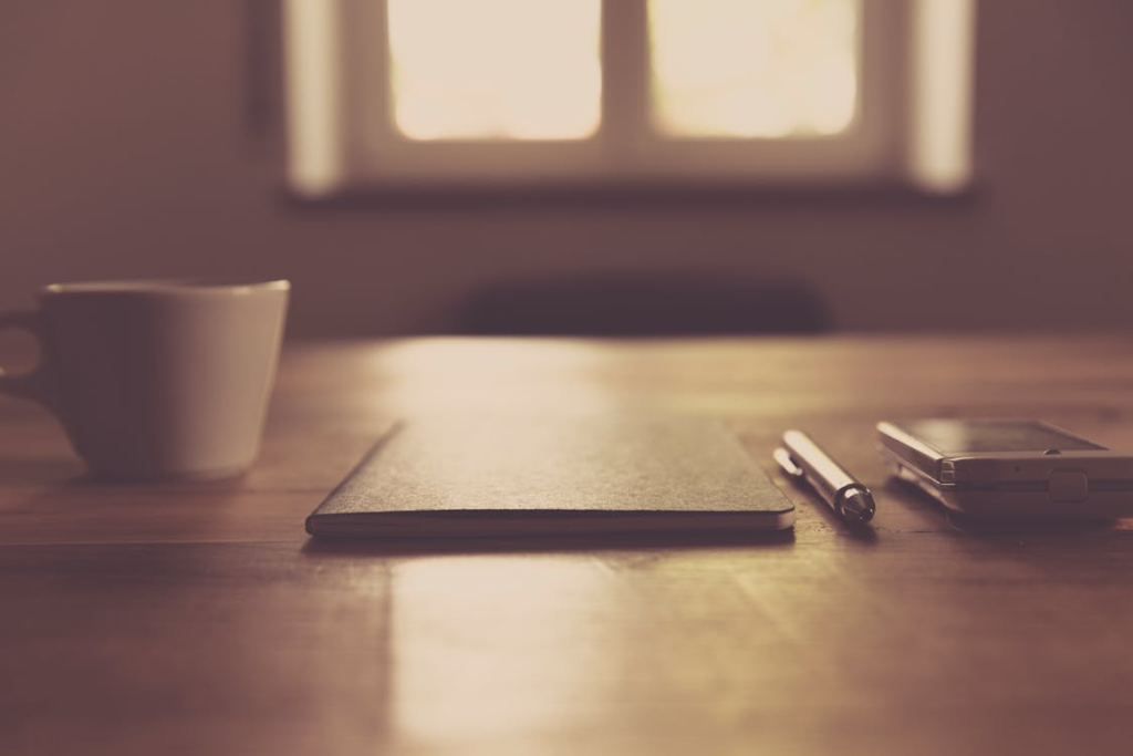 A minimal desk with a cup of coffee, a smartphone, and a notebook in natural light