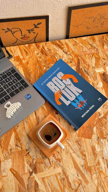 A wooden desk setup with a book, coffee, and laptop in a productive atmosphere