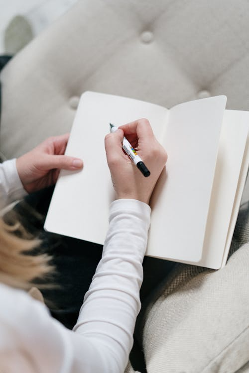 A person writing in a notebook while seated in an armchair in a calm indoor setting