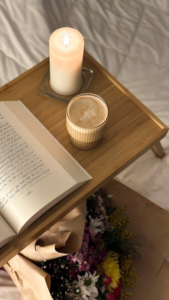 An inviting setup with an open book, a glass of coffee, and a lit candle for a relaxing reading session