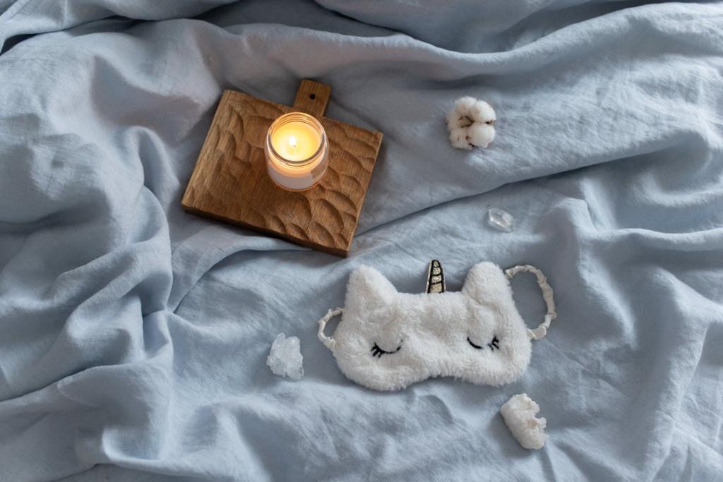A lit candle and soft linens arranged on a bed in a cozy bedroom setting