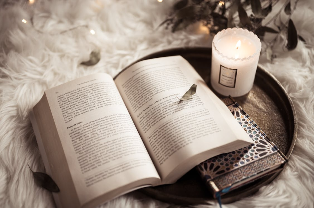 An open book, a lit candle, and a notebook arranged on a tray for an evening relaxation setup