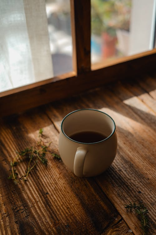 A warm cup of coffee on a rustic table near a window in soft morning light