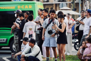 A diverse group of people gathered on a busy urban street corner with phones and cameras