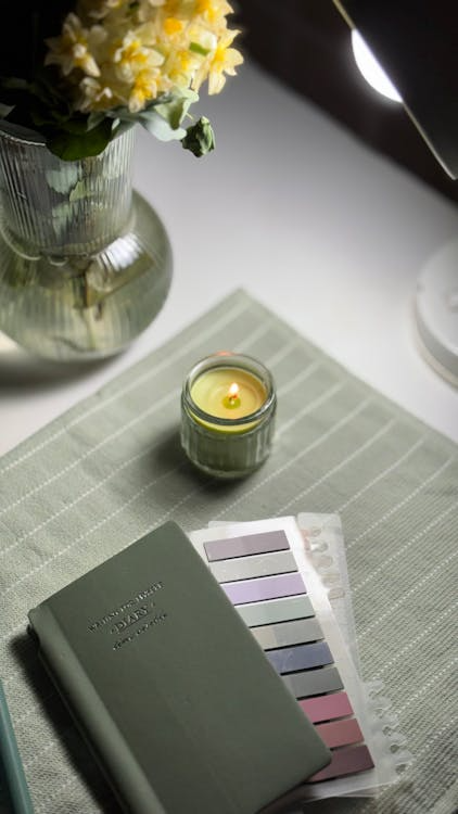 A cozy desk setup with a green planner, a lit candle, and a small vase of flowers