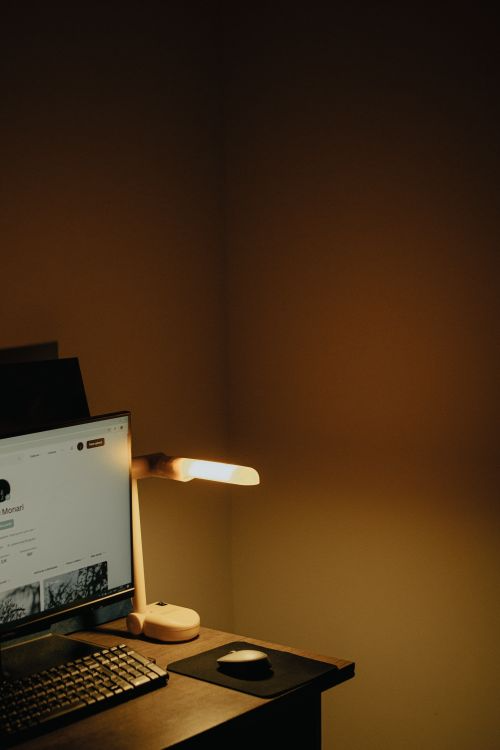 A cozy desk setup with a computer monitor and a warm-lit lamp casting soft ambient light across the workspace.