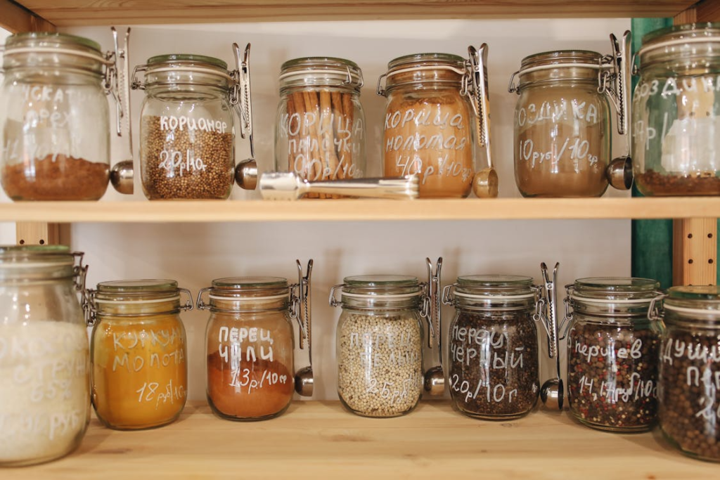 A wooden pantry shelf neatly organized with rows of labeled glass jars containing dry goods, spices, and ingredients.