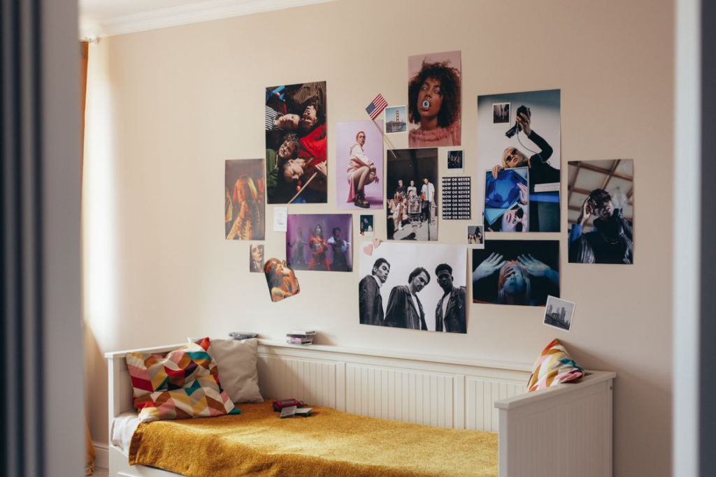  A bedroom wall covered with a colorful collage of artistic posters featuring varied designs, typography, and bold visual styles.