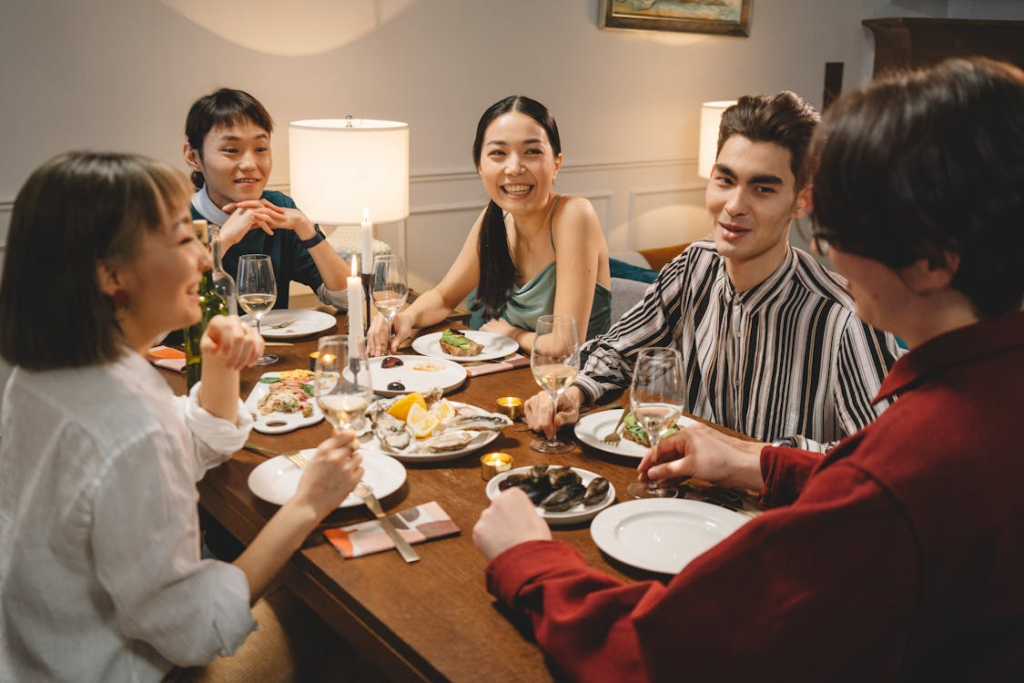 A group of friends smiling and dining together around a candlelit table in a warm, intimate setting.