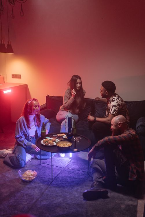 A small group of friends enjoying drinks and snacks together in a cozy living room setting at night.