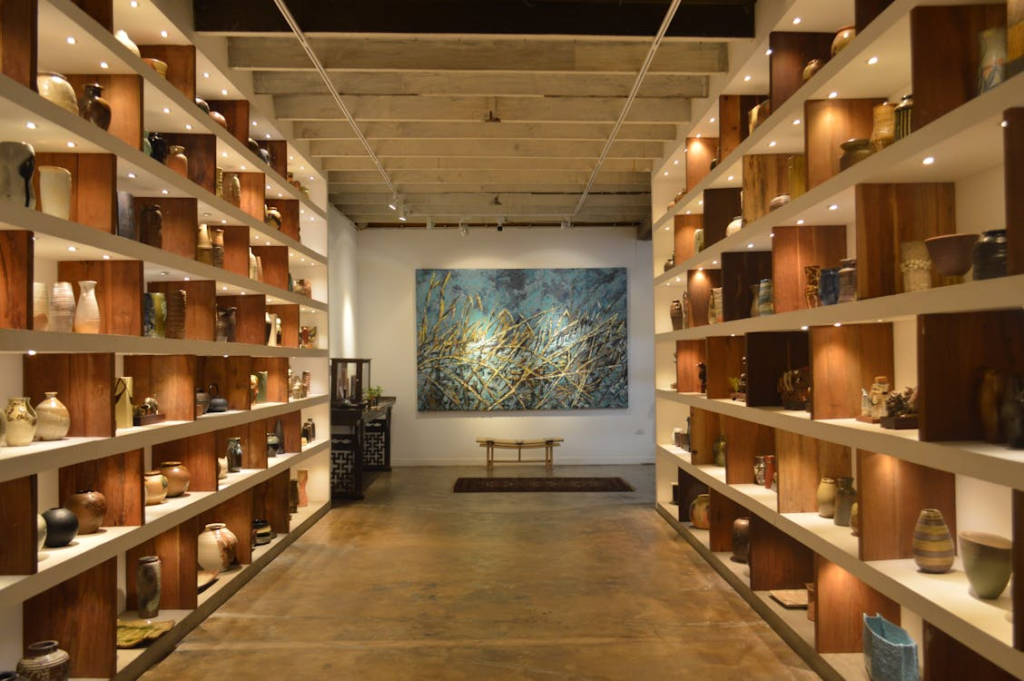  A modern art gallery interior featuring wooden shelves with pottery and a large abstract painting at the center.